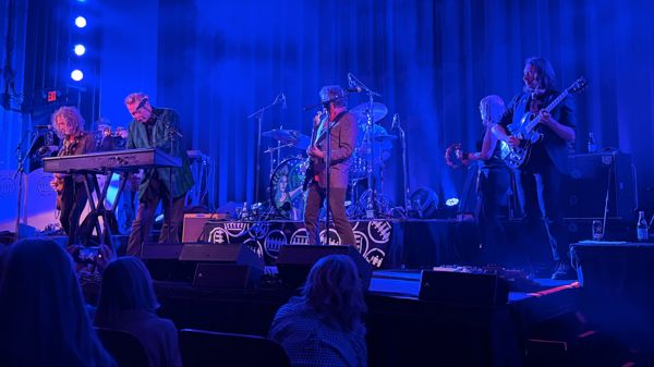Band performs on a blue-lit stage with keyboards, guitar, and drums at the Parkway Theater