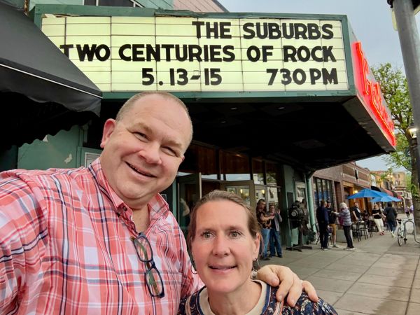 Two people take a selfie in front of the Parkway Theater marquee reading The Suburbs Two Centuries of Rock 5.13-15 730 PM
