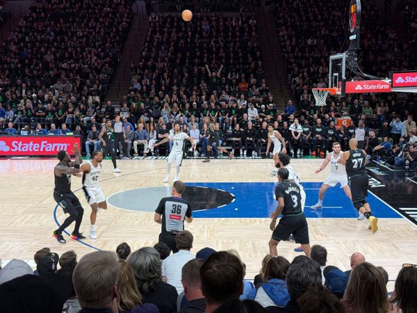 NBA playoff game at Target Center with players in black Timberwolves and white Spurs uniforms mid-play near the basket before a packed crowd.