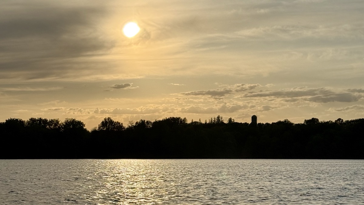 Golden sunset over a calm lake with a silhouetted tree line and water tower in the background